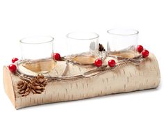 three wine glasses sitting on top of a wooden log with pine cones and red berries