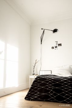 a bedroom with white walls and wood flooring has a black blanket on the bed