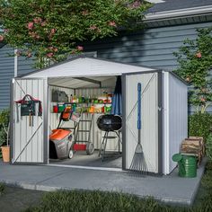 an outdoor storage shed with the door open and tools in it, next to some flowers