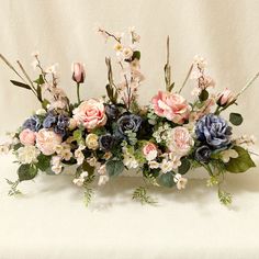 a bunch of flowers that are sitting on a white table cloth with some green leaves