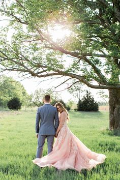 a bride and groom walking through the grass under a tree