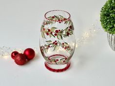 a glass vase sitting next to a christmas ornament on a white table with red ornaments