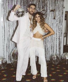 a man and woman posing for a photo in front of disco ball backdrop at a party