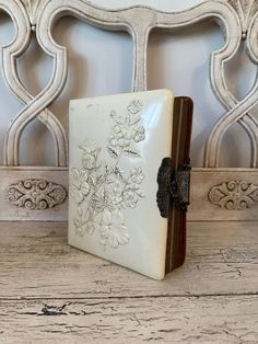 an old book with flowers on it sitting on a wooden table next to a white chair