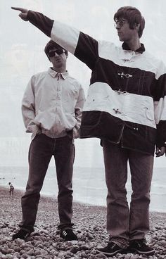 two young men standing on top of a rocky beach next to the ocean pointing at something