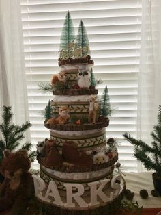 a tiered cake decorated with forest animals and pineconi trees is displayed in front of a window