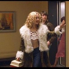 a woman in a fur coat is walking down the hallway with another man behind her