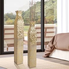 two gold vases sitting on top of a wooden floor next to a large window