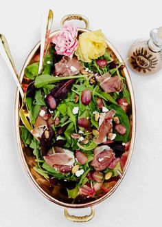 a salad in a bowl on a white surface with spoons and utensils