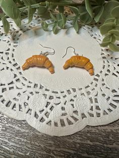 two orange caterpillar shaped earrings sitting on top of a white doily next to green leaves