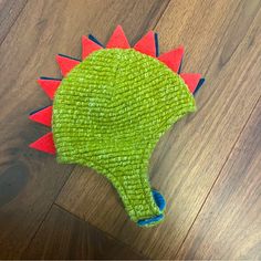 a green toy with red spikes on it's head sitting on a wooden floor