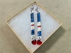 pair of red, white and blue earrings with heart shaped beads sitting on top of a square plate