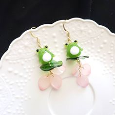 frog earrings with pink and green leaves hanging from gold earwires on a white plate