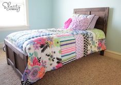 a bed with a colorful quilt on top of it next to a window and carpeted floor