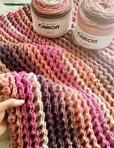 someone is crocheting yarn on top of a blanket with two jars of cake