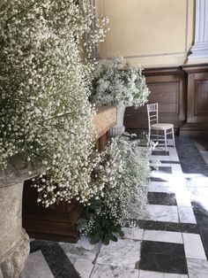 some white flowers are sitting in a vase on the floor next to a bench and chair