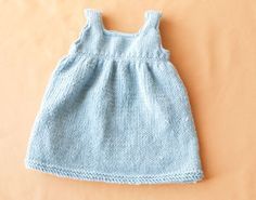 a blue knitted baby dress laying on top of a white surface with an orange wall in the background