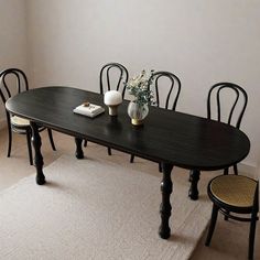 a dining room table with four chairs and a vase on the floor next to it