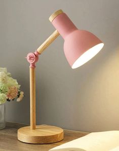 a pink desk lamp sitting on top of a wooden table next to a vase with flowers