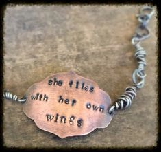 a silver bracelet with words on it that says she flies with her own wings,