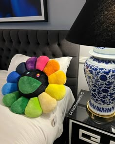 a bed with a colorful pillow on it next to a lamp and a large vase