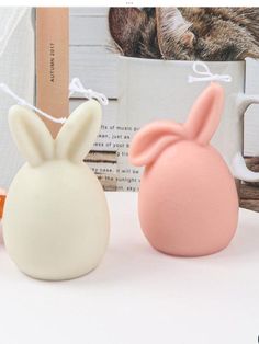 two bunny shaped candles sitting next to each other on a white table with a cat in the background