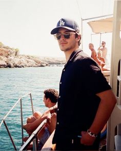 a man standing on top of a boat in the ocean next to another man wearing sunglasses