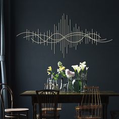 a dining room table with vases and flowers on it, against a dark blue wall