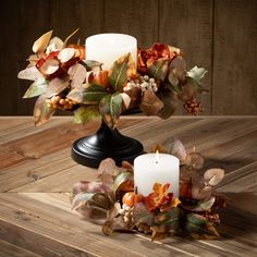 two candles are sitting on a table with autumn leaves and other decorations around the candle