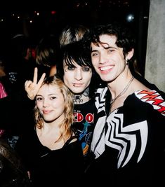 three young people posing for the camera at a party with one holding up his peace sign