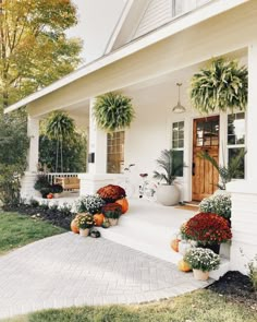 a white house with potted plants and pumpkins on the front porch, along with two bikes