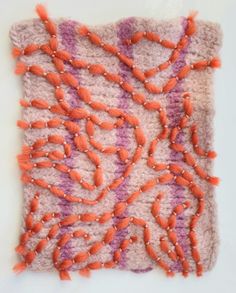 an orange and pink piece of art with beads on it's edges, sitting on a white surface