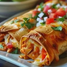 two burritos on a plate with salsa and tomatoes