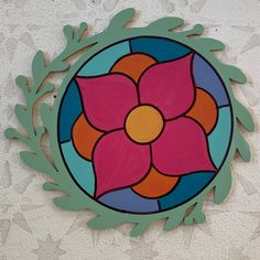 a circular stained glass window with leaves and flowers on the side of a white wall