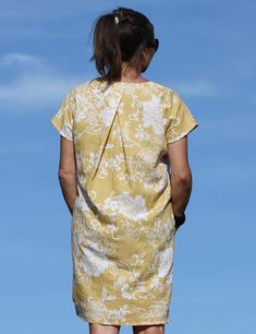 a woman in a yellow dress is standing on the beach looking at the water with her back to the camera