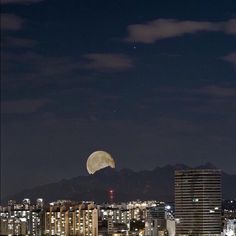 the full moon is seen in the sky over a cityscape with tall buildings