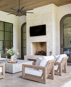 an outdoor living room with white furniture and a flat screen tv mounted above the fireplace