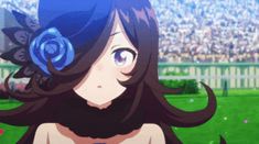 a woman with long dark hair wearing a blue flower in her hair, standing in front of a stadium