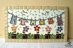 a mosaic tile wall hanging with clothes on a line and flowers in the grass next to it