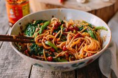 a bowl filled with noodles and vegetables on top of a wooden table next to chopsticks