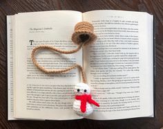 an open book with a crocheted teddy bear hanging from it's side