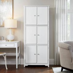 a white cabinet in a living room next to a chair and table with a lamp on it