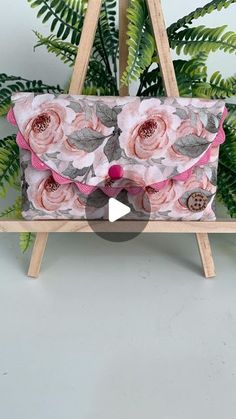 a pink flowered purse sitting on top of a wooden easel next to a plant