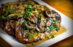 the steak is covered in mushrooms and gravy on top of a white plate