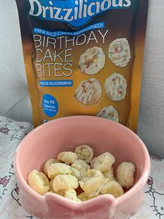 a pink bowl filled with cake bites next to a bag of frozen birthday cookies on a table