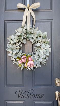 a wreath with flowers is hanging on the front door and welcome sign above it that says welcome