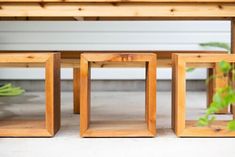 three wooden frames sitting on top of a cement floor next to a green plant in front of a white house