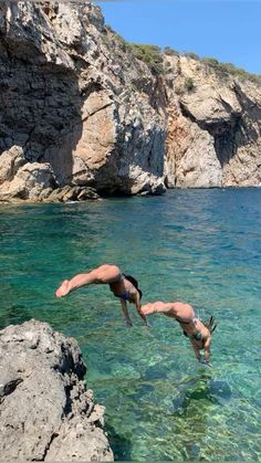 two people diving into the ocean from rocks