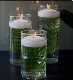 three glass vases filled with candles on top of a black table next to a plant