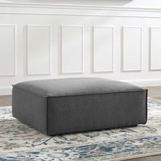 a grey ottoman sitting on top of a rug in front of a white wall and floor